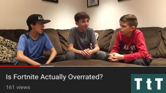 Three young boys are seated on a brown couch in a living room, engaged in a discussion, with one boy wearing a blue shirt and cap, another in a gray shirt, and the third in a red shirt with "ALLNT" printed on it.