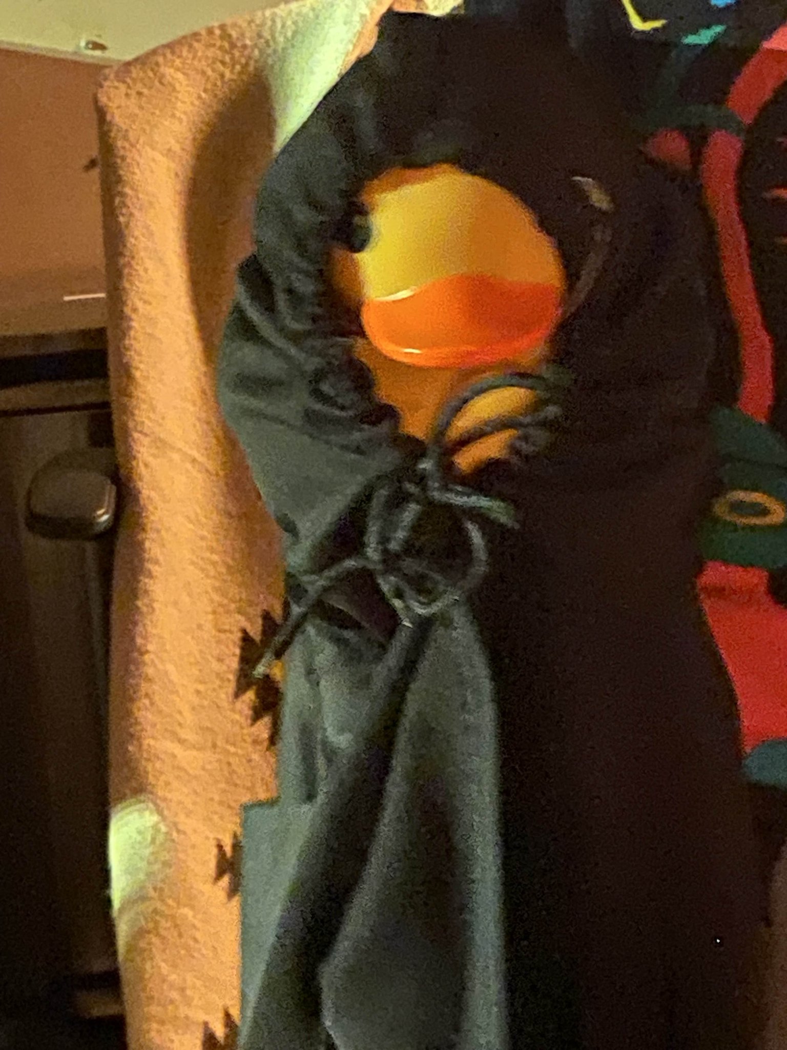 A yellow rubber duck with an orange beak is tucked inside a black drawstring bag. The bag is partially open, revealing the duck's face, and is set against a textured tan and patterned background.